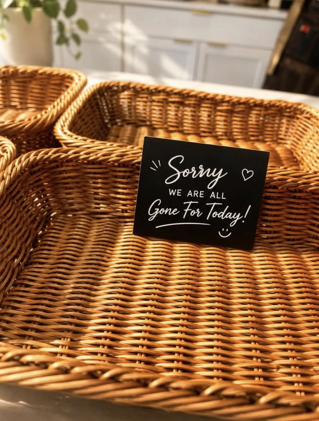 Empty wicker bread baskets in afternoon light with a small chalkboard card reading “Sorry, we are all gone for today!”