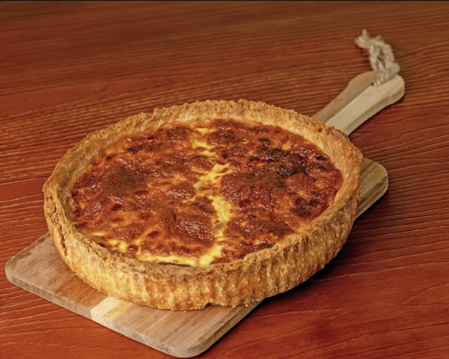 A deep golden quiche on a wooden serving board.